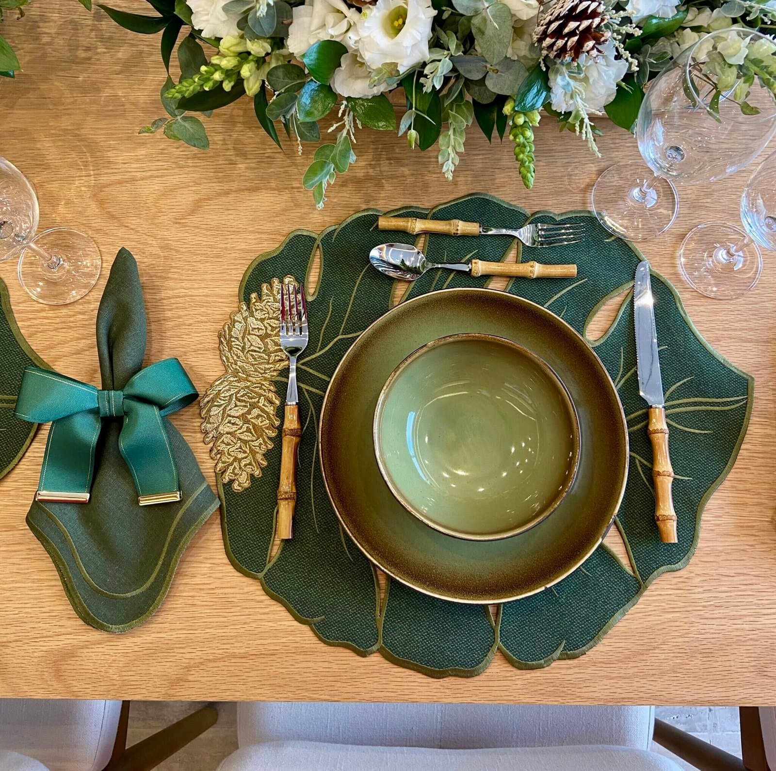 Mesa de Natal com lugar americano verde recortado em folhas, guardanapo com laço e louça verde-oliva