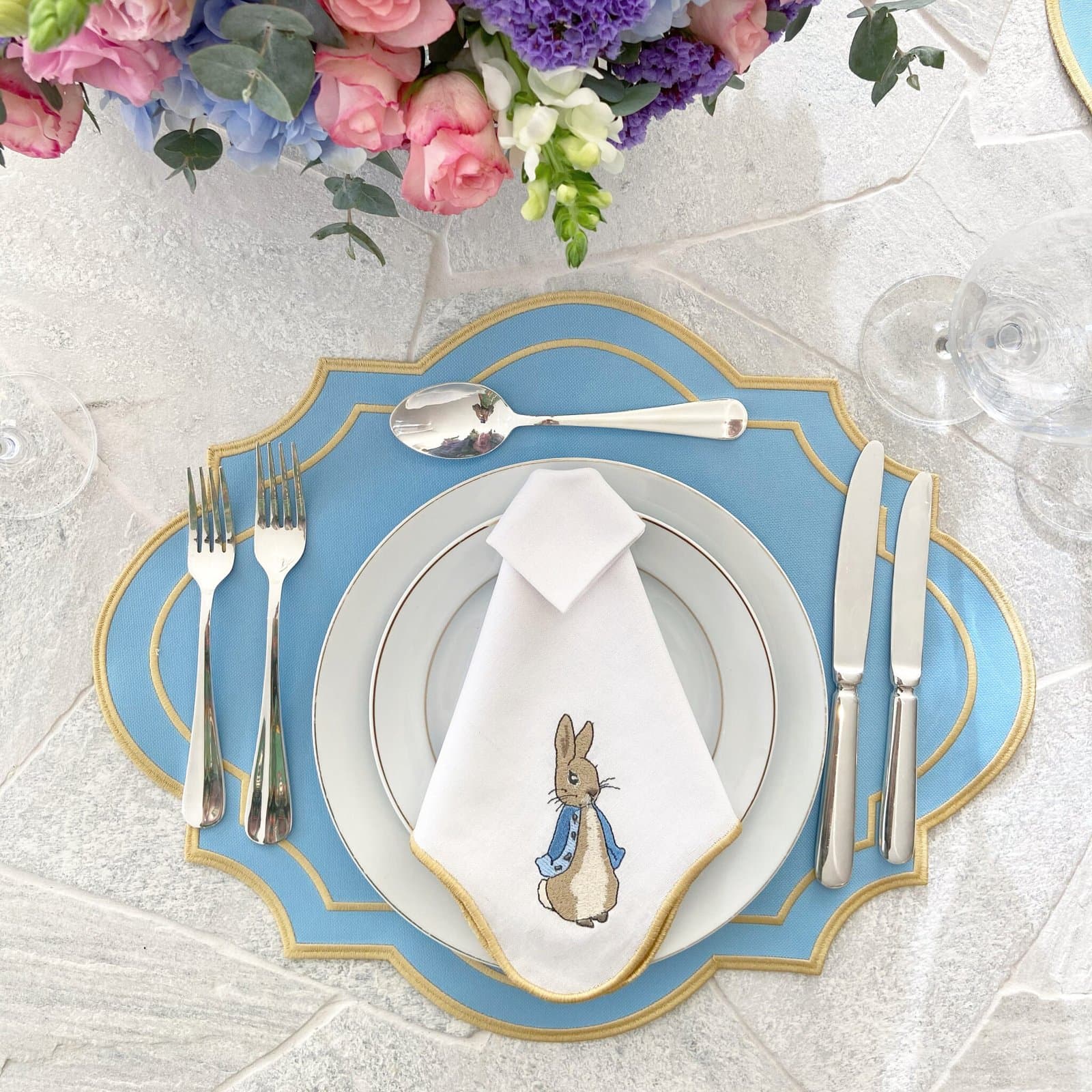 Mesa de Páscoa com lugar americano azul céu com borda dourada e guardanapo branco com coelho bordado